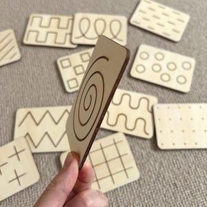 May include: A set of wooden tracing cards featuring a variety of patterns, such as a spiral, zigzags, squares, and dots. These cards are ideal for helping children develop their fine motor skills and hand-eye coordination.