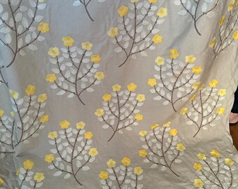 May include: Beige fabric with a repeating pattern of embroidered yellow flowers and white leaves on branches.