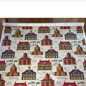 May include: A white fabric with a repeating pattern of red, blue, and gold buildings. The buildings are drawn in a vintage style with architectural details. The background is a cream color with a faint pattern of architectural plans.