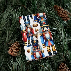 May include: A wrapped gift with a festive design featuring colorful nutcracker soldiers on a white background. The wrapping paper is tied with twine and surrounded by pine needles and pine cones, creating a holiday theme.