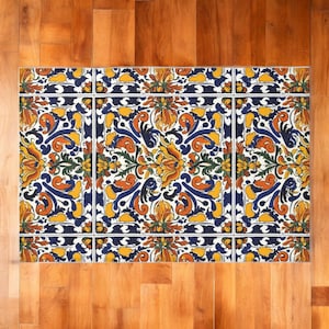 May include: Rectangular decorative mat with a floral design. The mat features a white background with a repeating pattern of orange, yellow, and blue flowers and leaves. A dark blue border frames the design.