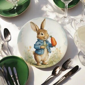 May include: A white ceramic plate with a watercolour illustration of a rabbit in a blue jacket, holding a carrot. The plate is surrounded by green plates, cutlery, and glassware, creating a festive table setting.