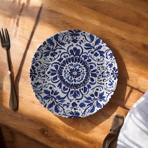 May include: A white and blue decorative plate with a floral design. The plate is round and features a detailed pattern of blue flowers and leaves against a white background. A dark metal fork is on the left side of the plate.