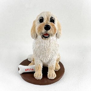 May include: A white ceramic figurine of a dog sitting with a bone that says "BELLA" on it.