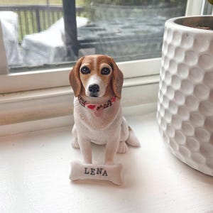 May include: A ceramic figurine of a beagle dog wearing a red and white collar with a name tag that says "Lena".