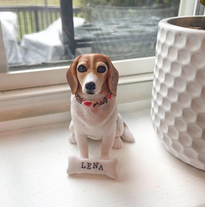 May include: A ceramic figurine of a beagle dog wearing a red and white collar with a name tag that says "Lena".