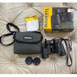 May include: A set of Bushnell Spectator Series binoculars with a carrying case, lens caps, and original packaging. The binoculars are black with a neck strap. The case is olive green with the Bushnell logo. The box is yellow and black.