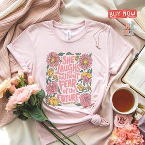 May include: Pink t-shirt with a floral design and the text "She laughs without fear of the future, Proverbs 31:25".