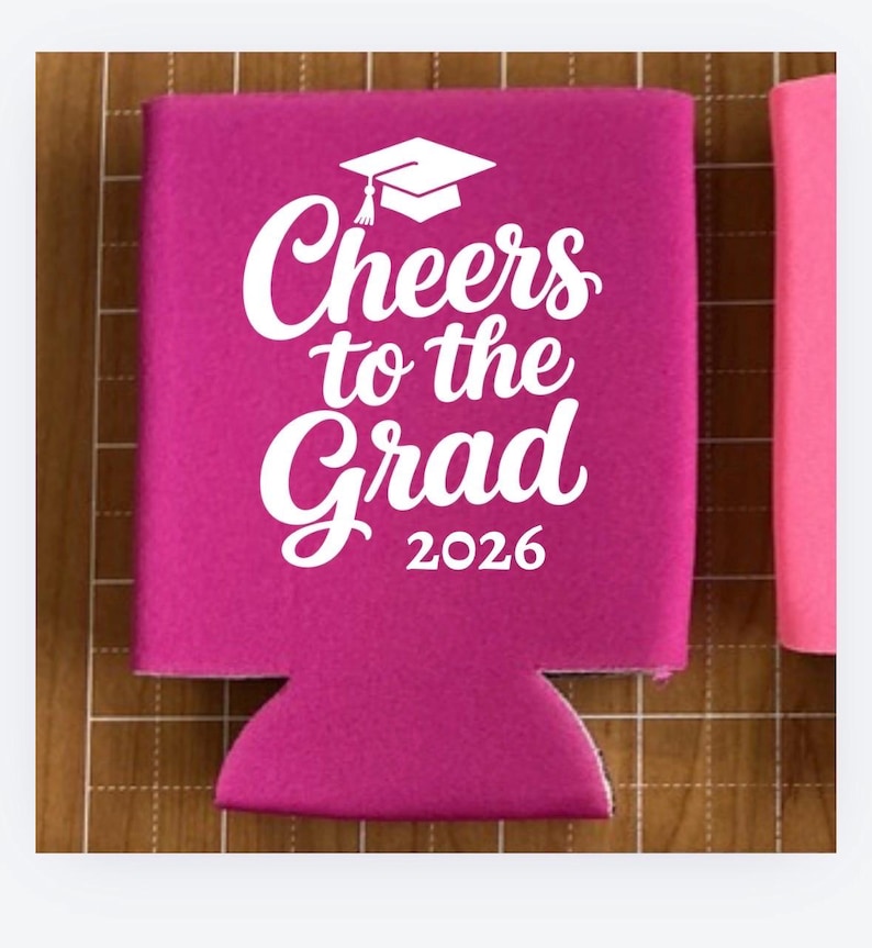 May include: A magenta-colored can cooler with the text "Cheers to the Grad 2026" in white script and a graduation cap graphic. The cooler is designed to hold a standard-sized can or bottle.