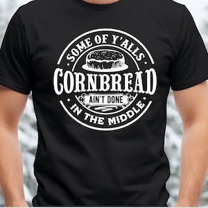 May include: Black t-shirt with a white circle graphic that says "Some of y'alls cornbread ain't done in the middle".