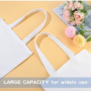 May include: Two white canvas tote bags with long handles, ideal for carrying items. The bags are displayed on a yellow background, with a bouquet of pink and yellow flowers in the background. The text "LARGE CAPACITY for widely use" is visible at the bottom.