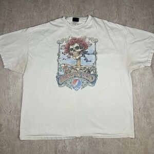 May include: White t-shirt with a graphic print of a skeleton with a skull head wearing a flower crown. The graphic includes the text "Grateful Dead" and a colorful swirl design.