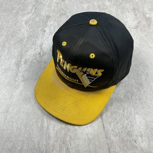 May include: Black and yellow baseball cap with the Pittsburgh Penguins logo embroidered on the front.