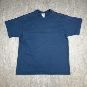 May include: A solid navy blue t-shirt with a crew neck and short sleeves. The shirt is made of a soft material and has a tag at the neckline. The shirt is laid flat on a gray surface.