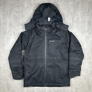 May include: Black hooded jacket with a zip fastening and the Patagonia logo on the chest. The jacket features a hood and two side pockets. The jacket is designed for outdoor activities and is made of a durable, water-resistant material.