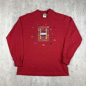 Puede incluir: Una camiseta roja de manga larga con cuello alto. La parte delantera de la camiseta presenta un diseño geométrico colorido con detalles azules, amarillos y blancos en un patrón rectangular, rodeado de formas más pequeñas. La camiseta es de material suave.