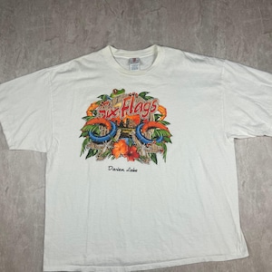 Könnte beinhalten: Weißes T-Shirt mit einem bunten Six Flags Darien Lake-Motiv, das einen Frosch, Palmen und eine Achterbahn zeigt. Das Motiv ist von einem blauen und weißen Seilmuster umgeben.
