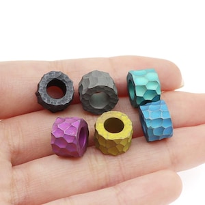 May include: Six different coloured metal beads with a textured surface. The beads are in a variety of colours, including black, blue, green, yellow, and purple.