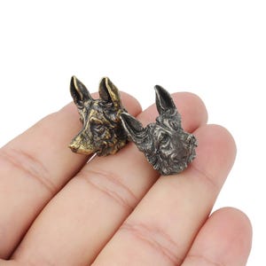 May include: Two metal dog head drawer pulls, one in gold and one in silver. The dog heads are facing forward with their mouths closed.