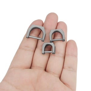 May include: Three silver metal D-ring clasps of different sizes. The rings are smooth and have a polished finish.