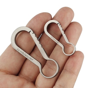 Puede incluir: Dos llaveros de titanio con un borde dentado y la palabra "TITANIUM" grabada en cada uno.