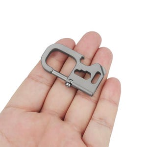 Pode incluir: Um chaveiro multiferramentas de metal prateado com um abridor de garrafas, uma chave de fenda plana e um mosquetão.