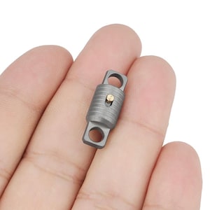 May include: A small, grey metal swivel clip with a gold pin. The clip is designed to attach to a keychain or other items.