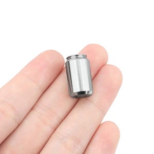 May include: A small, silver, cylindrical container with a smooth, metallic finish. The container is about the size of a standard soda can.