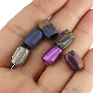 May include: Six different colored metal beads, each with a unique pattern and finish. The beads are arranged in a hand, with the purple bead in the center.