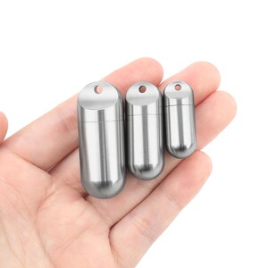 Puede incluir: Tres pequeños recipientes cilíndricos plateados de diferentes tamaños. Cada uno tiene una parte superior redondeada con un pequeño agujero y una tapa de rosca. Los recipientes se sostienen en la mano de una persona sobre un fondo blanco.