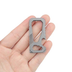 May include: A silver-coloured multi-tool keychain with a bottle opener, a loop for attaching keys, and a small flathead screwdriver.