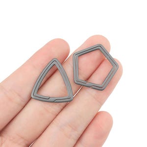 Puede incluir: Dos llaveros de metal, uno con forma de triángulo y el otro con forma de pentágono. Ambos llaveros son de color plateado.