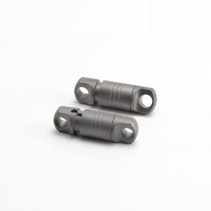 May include: Two small, cylindrical metal objects with a matte gray finish. Each object has a hole at both ends and a ridged design in the middle. The objects are likely components or hardware.