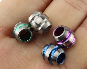 May include: Four titanium beads with different coloured accents. The beads are round with a grooved texture and have a polished finish. The colours are green, purple, blue, and silver.