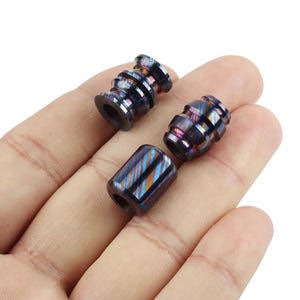 May include: Three colorful metal beads with a swirling pattern. The beads are made of stainless steel and have a blue, purple, and gold color scheme.