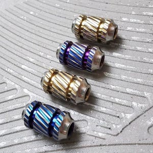 May include: Four metal fidget toys with a grooved design. The toys are in different colours: gold, purple, blue, and blue with a silver accent.