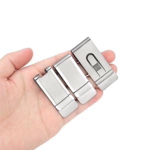 Puede incluir: Se muestran tres clips de dinero plateados. Cada clip tiene forma rectangular con un mecanismo de resorte. Los clips están hechos de un material metálico brillante y están diseñados para sujetar de forma segura efectivo y tarjetas.