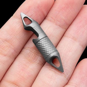 Könnte beinhalten: Ein silberfarbener Schlüsselanhänger aus Metall mit einem Flaschenöffner, einer Schlaufe zum Anbringen von Schlüsseln und einem spitzen Ende.