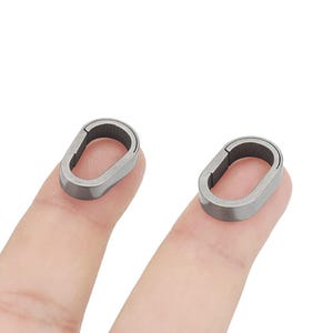Può includere: Due anelli ovali in argento con un piccolo spazio su un lato. Gli anelli sono mostrati su due dita.