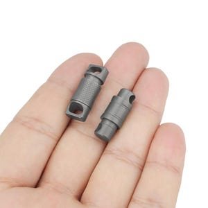 May include: Two silver metal clips with a textured surface. The clips are designed to be used for attaching items to a keychain or lanyard.