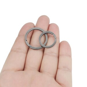 May include: Two silver metal key rings, one larger than the other, are held in a hand. The rings are both circular and have a smooth, polished finish.