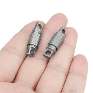 May include: Two silver metal keychains with a swiveling design. The keychains are held in a hand.