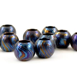 May include: A group of spherical beads with a swirling, iridescent finish. The beads feature a mix of blues, purples, and gold, creating a unique appearance. These decorative beads are suitable for jewellery making or craft projects.
