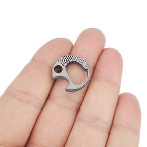 May include: A silver titanium bottle opener keychain with a textured design. The keychain has a small hole for attaching to a key ring.