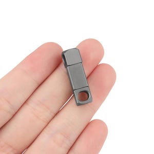 Puede incluir: Un llavero de metal plateado con un bucle en un extremo y una pequeña abertura redonda en el otro extremo.