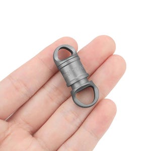 Puede incluir: Un mosquetón giratorio plateado con el texto "SIGN 1104" grabado en el lateral.