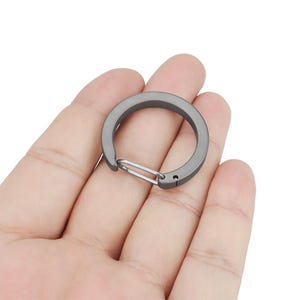 May include: A gray metal key chain with a spring-loaded clip. The clip is open and ready to attach to a key ring or other item.