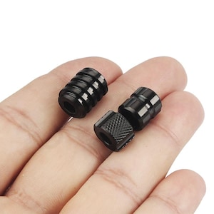 Puede incluir: Tres tapas de metal negro para un bolígrafo vape. Las tapas tienen diferentes diseños, una es acanalada, otra es lisa y otra tiene un patrón moleteado.