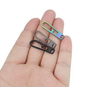 May include: Three metal keychains, one black, one iridescent green, and one iridescent blue, with a loop on one end and a hook on the other end.