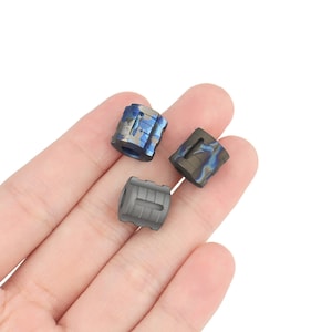 May include: Three small, cylindrical fidget toys made of titanium. The toys are in different colours and patterns: blue and white, grey, and black and blue.